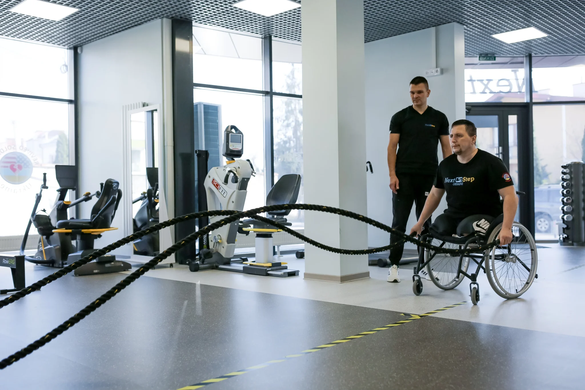 Rehabilitationsraum: Ein Mann im Rollstuhl übt neben einem Trainer