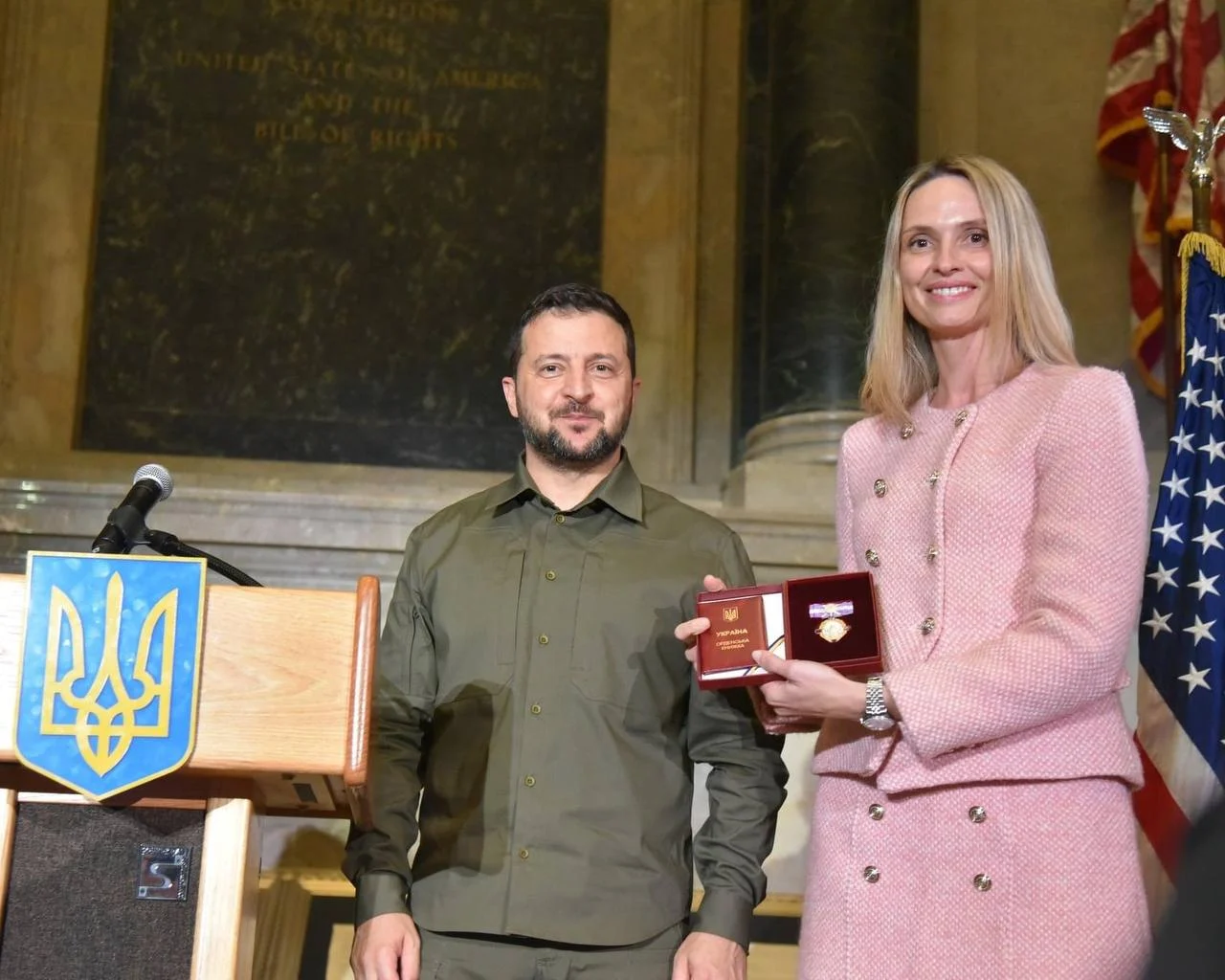 Preisverleihung: Eine Frau in rosa Jacke hält eine Auszeichnung neben einem Mann im Militärhemd